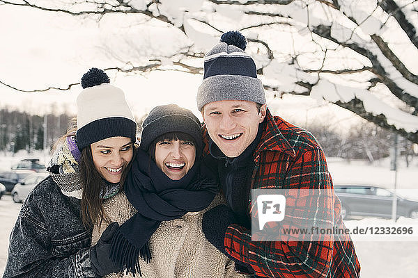 Cheerful friends in warm clothing embracing at park during winter