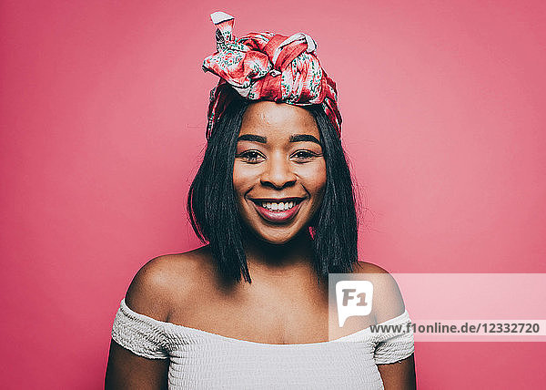 Portrait of smiling woman wearing head tie over pink background