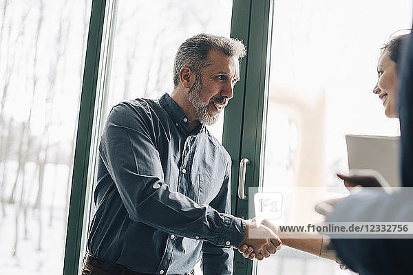 Mature businessman greeting female coworker in meeting at office