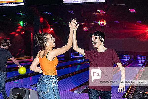 Cheerful friends giving high-five on parquet floor at bowling alley