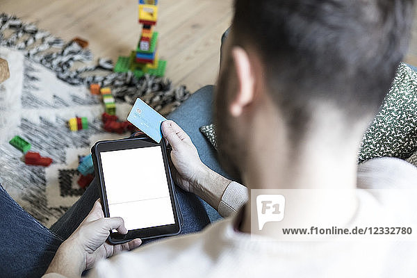 Close-up of young man shopping on digital tablet through credit card while relaxing at home