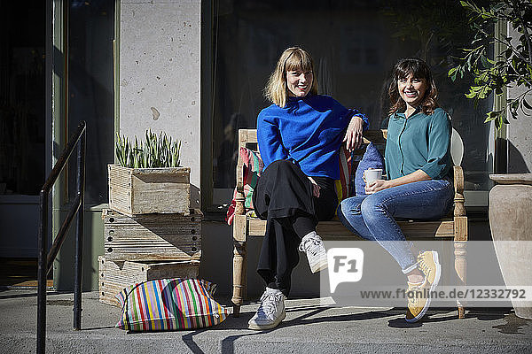 Full length portrait of smiling owners sitting on bench outside store