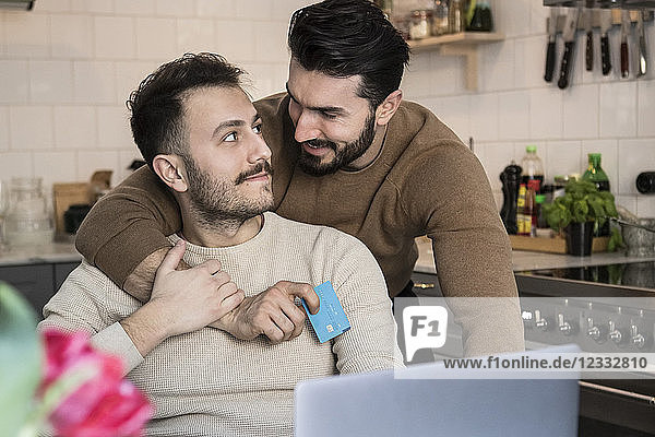 Romantic gay couple doing online shopping through laptop in kitchen at home
