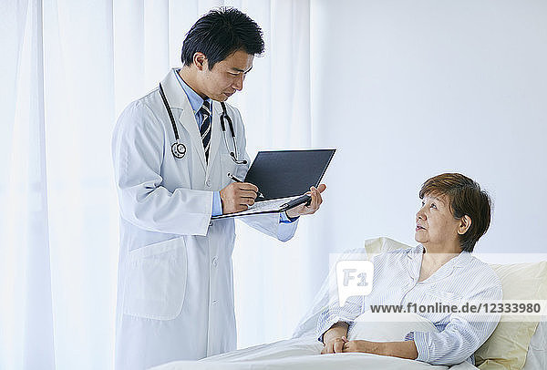 Japanischer Arzt mit einem Patienten im Bett