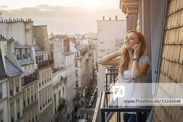 France  Paris  portrait of smiling woman on the phone standing on balcony in the evening
