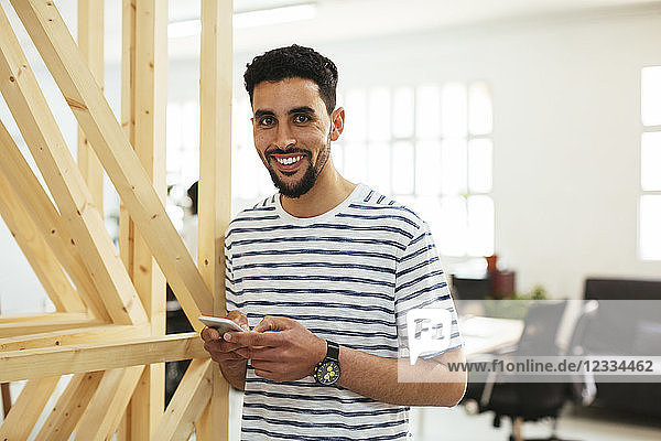 Portrait of smiling young man with cell phone in office