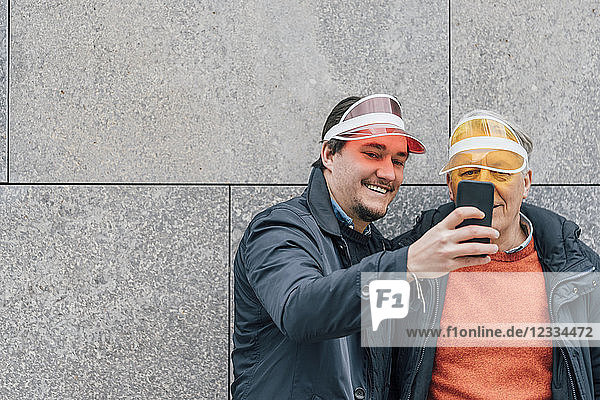 Smiling young man and senior man wearing sun visors taking a selfie