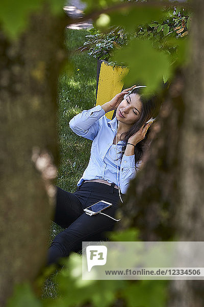 Young woman sitting on a meadow listening music with headphones and cell phone