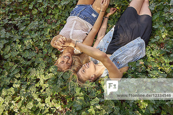 Two happy best friends lying on ground covered with ivy