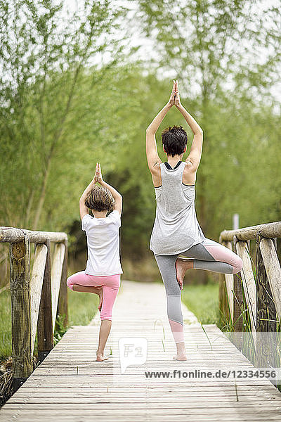 Rear view of mother and daughter doing yoga on boardwalk