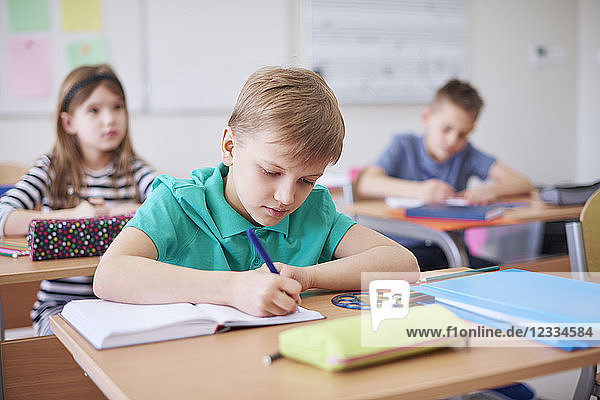Schoolboy writing in exercise book in class