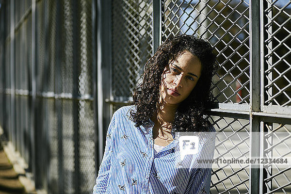 Portrait of beautiful young woman leaning against a fence