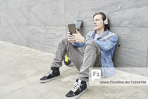 Young man with skateboard sitting on ground  using digital tablet