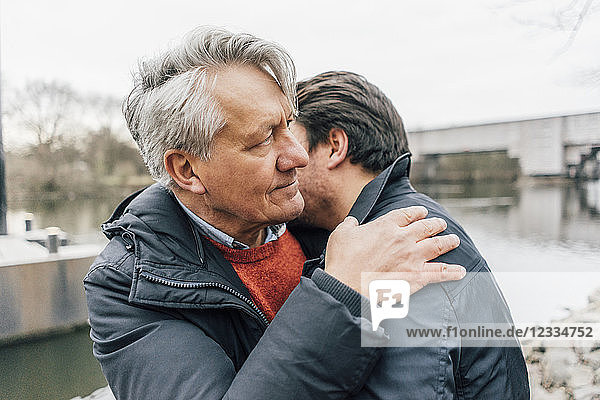Young man and senior man embracing at the riverside