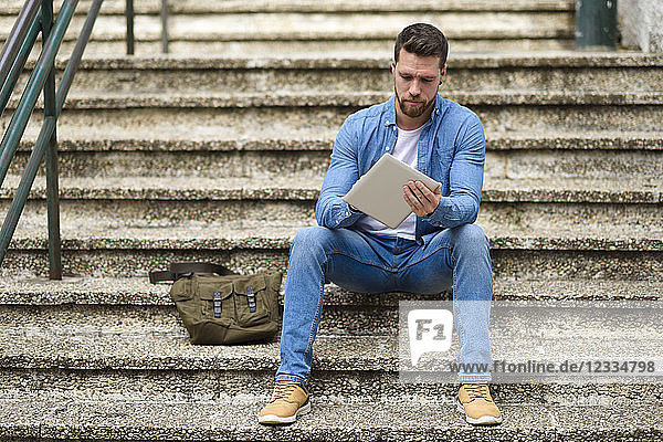 Young man sitting on stairs  working  using digital tablet