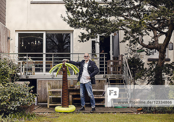 Senior businessman standing in his garden  holding a rubber palm  dreaming of vacations