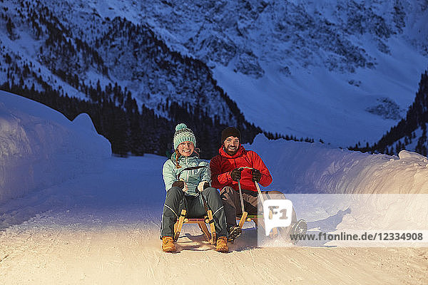 Happy couple sledding in snow-covered landscape at night