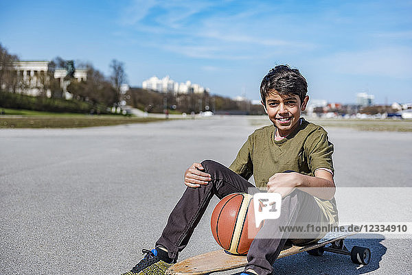 Portrait of smiling boy with longboard and basketball outdoors