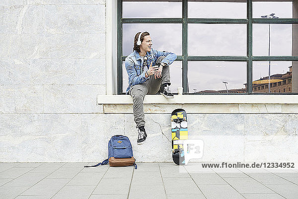 Young man sitting on window sill  waiting  using smartphone