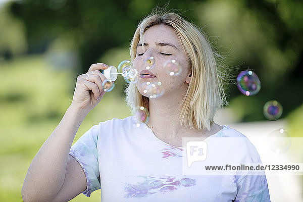 Young blonde woman blowing soap bubbles outdoors