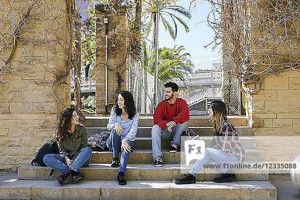 Four happy friends sitting on stairs outdoors talking