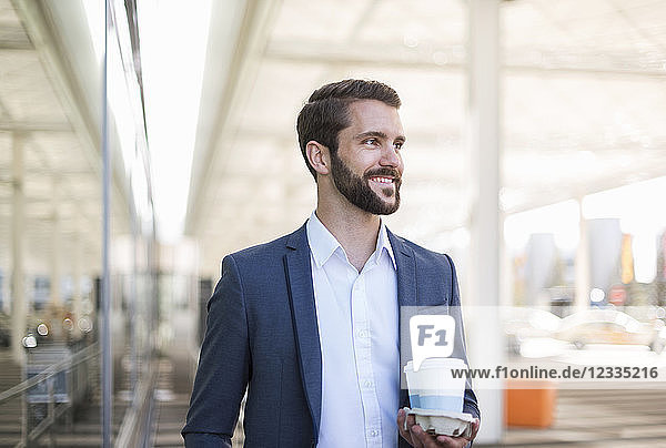 Smiling young businessman holding tray with takeaway coffee