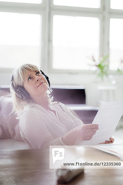 Relaxed mature businesswoman wearing headphones at desk looking up