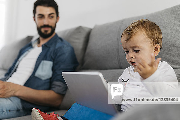 Father sitting on couch while the daughter watching the tablet