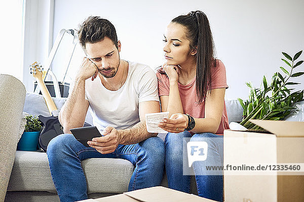Serious couple sitting on couch in new home checking bills