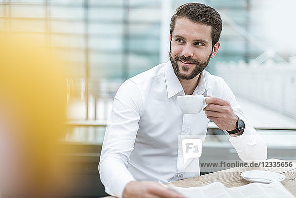 Smiling young businessman with newspaper and cup of coffee in a cafe