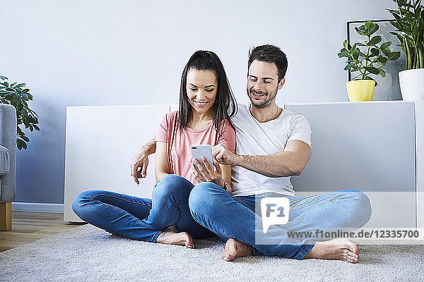 Couple sitting on floor and using smartphone