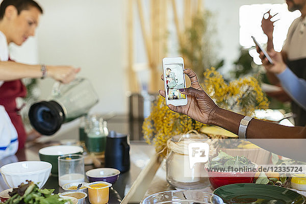 Close-up of woman taking smartphone picture of instructor working in a cooking workshop