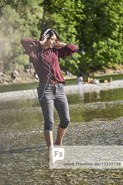 Young woman listening music with headphones and cell phone dancing at riverside