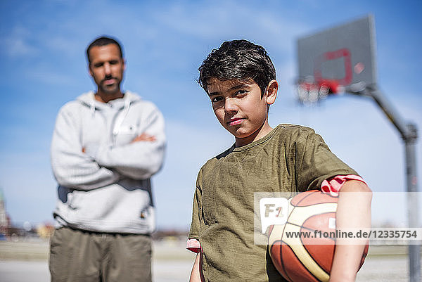 Portrait of boy posing with father on basketball court outdoors