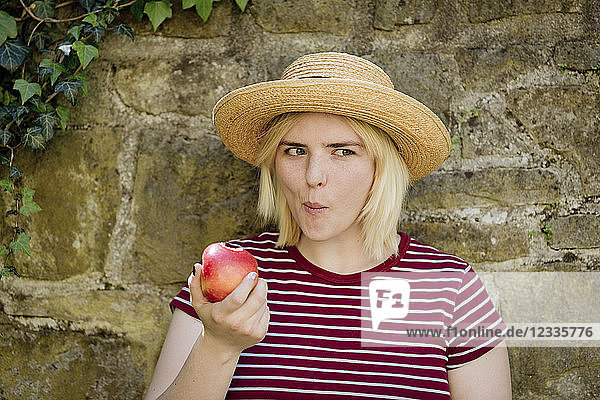 Portrait of young blonde woman with sun hat eating apple