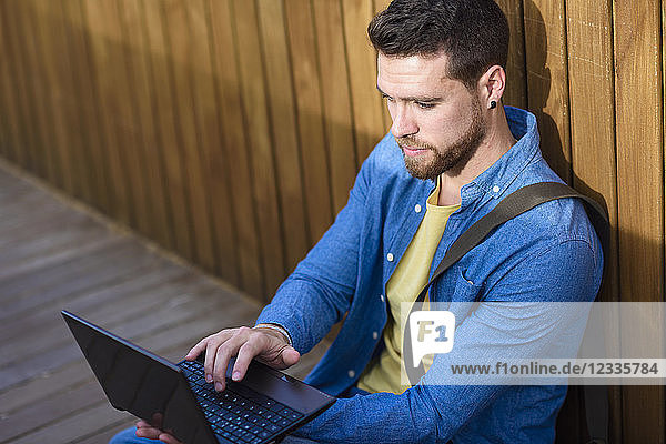 Young man sitting on footbridge using mini laptop