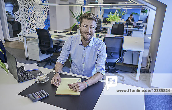Portrait of smiling businessman sitting at desk in open-plan office