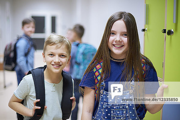 Portrait of smiling schoolboy and schoolgirl at lockers in school