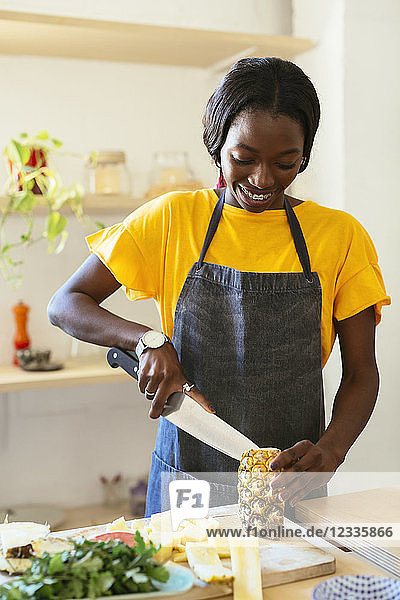 Smiling woman cutting pineapple in kitchen
