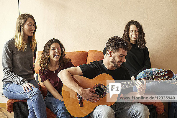 Happy freinds listening to man playing guitar on couch