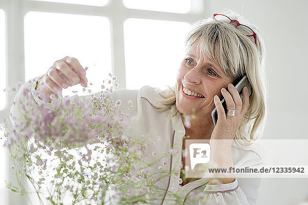 Smiling mature woman on cell phone caring for flowers