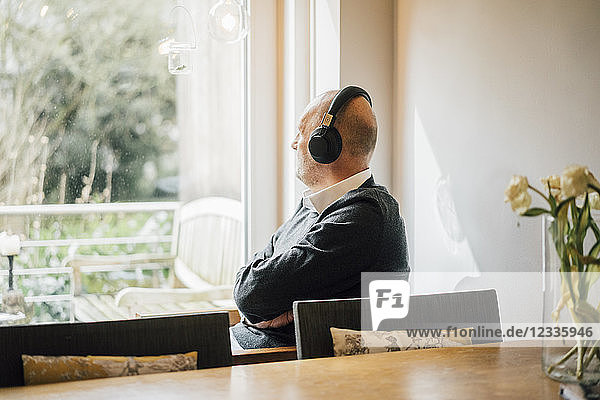 Senior man sitting at home  listening music  looking out of window