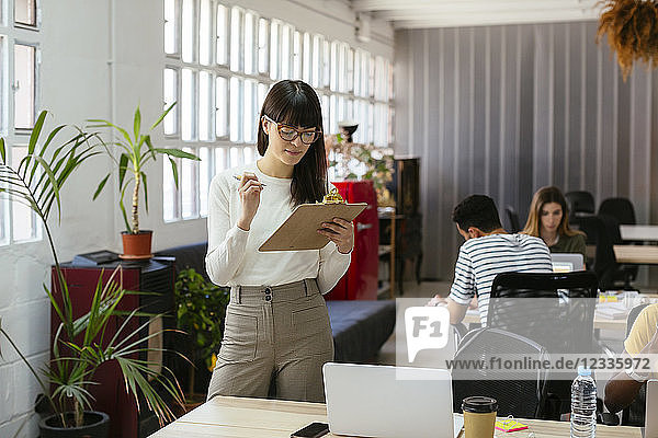 Woman with clipboard among colleagues in office