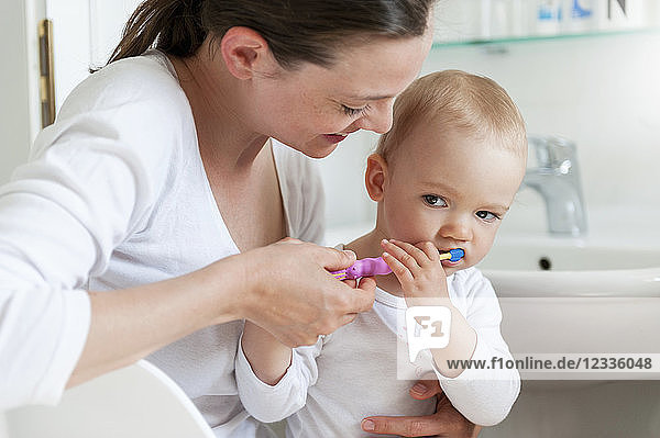 Mother brushing baby's teeth in bathroom