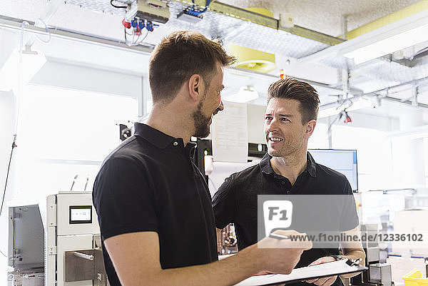 Two men with clipboard talking in factory