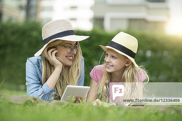 Happy mother and daughter with book and smartphone in urban city garden