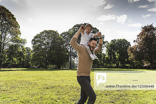 Happy father carrying son on shoulders in a park