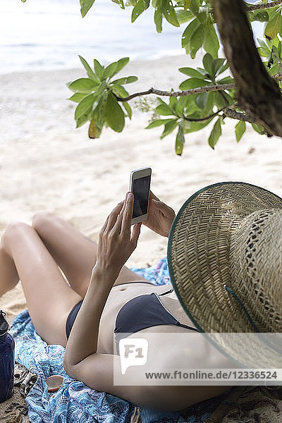 Young lying woman on the beach  using smartphone
