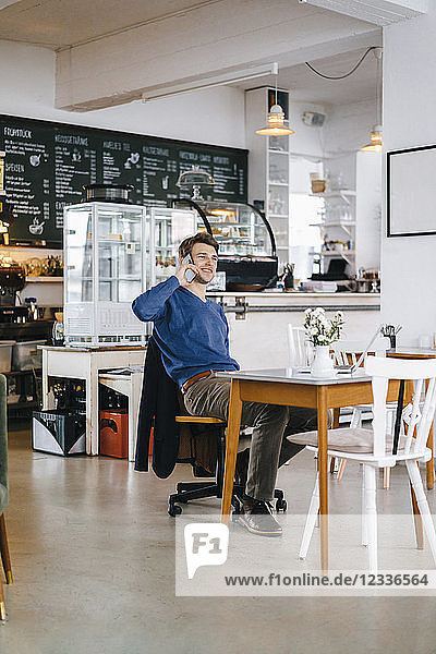 Smiling man in a cafe with laptop on cell phone
