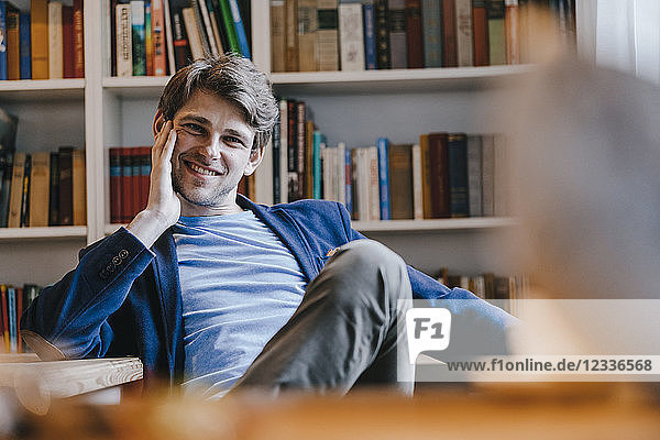 Portrait of smiling man sitting at bookshelf